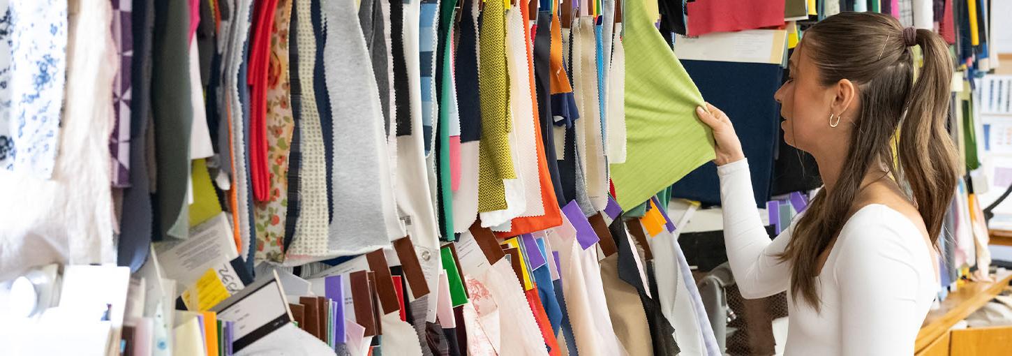 A woman browses through hangers of fabric.